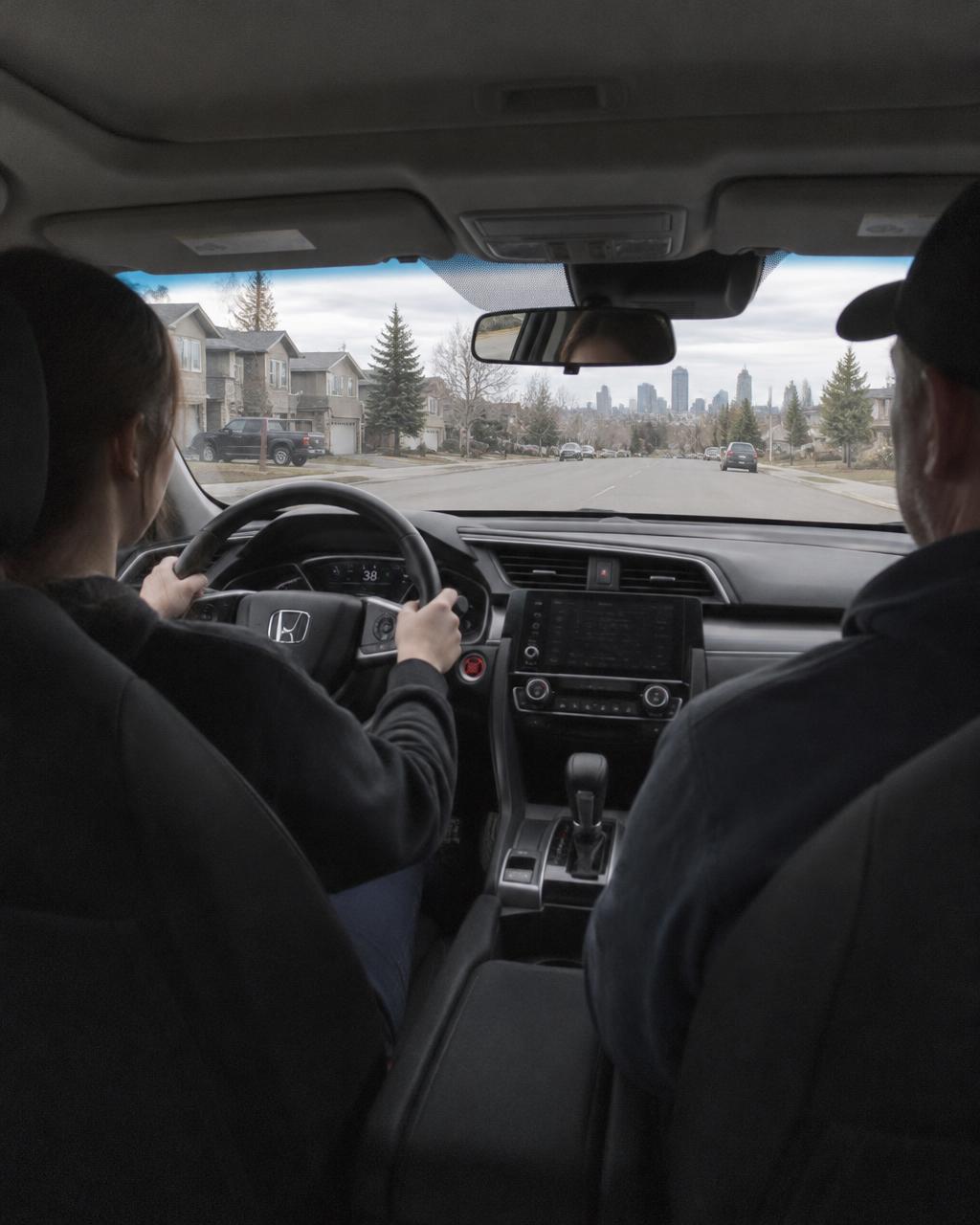 Student driver with both hands on the wheel of a Honda Civic, eyes on the road, instructor in the passenger seat